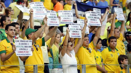 Protesters hold signs before the Confederations Cup Group A soccer match between Brazil and Mexico at the Estadio Castelao in Fortaleza